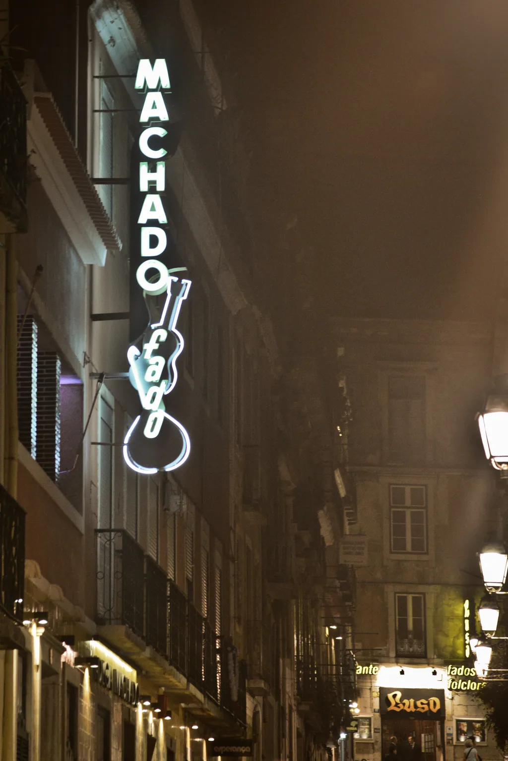 Rua estreita do Bairro Alto com nevoeiro e o néon da Adega Machado ao fundo