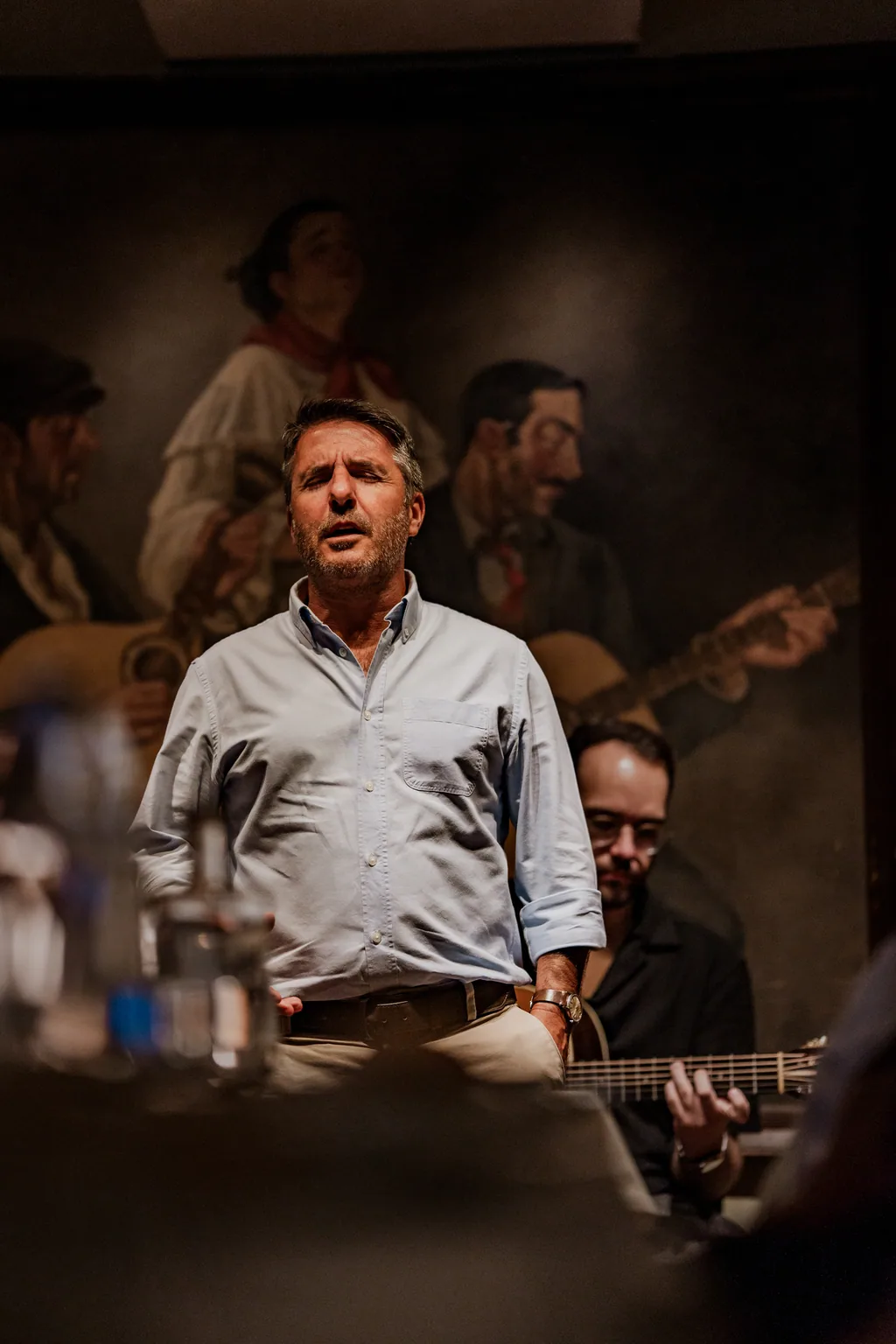 Fadista a cantar na sala, diante do quadro, com os músicos atrás