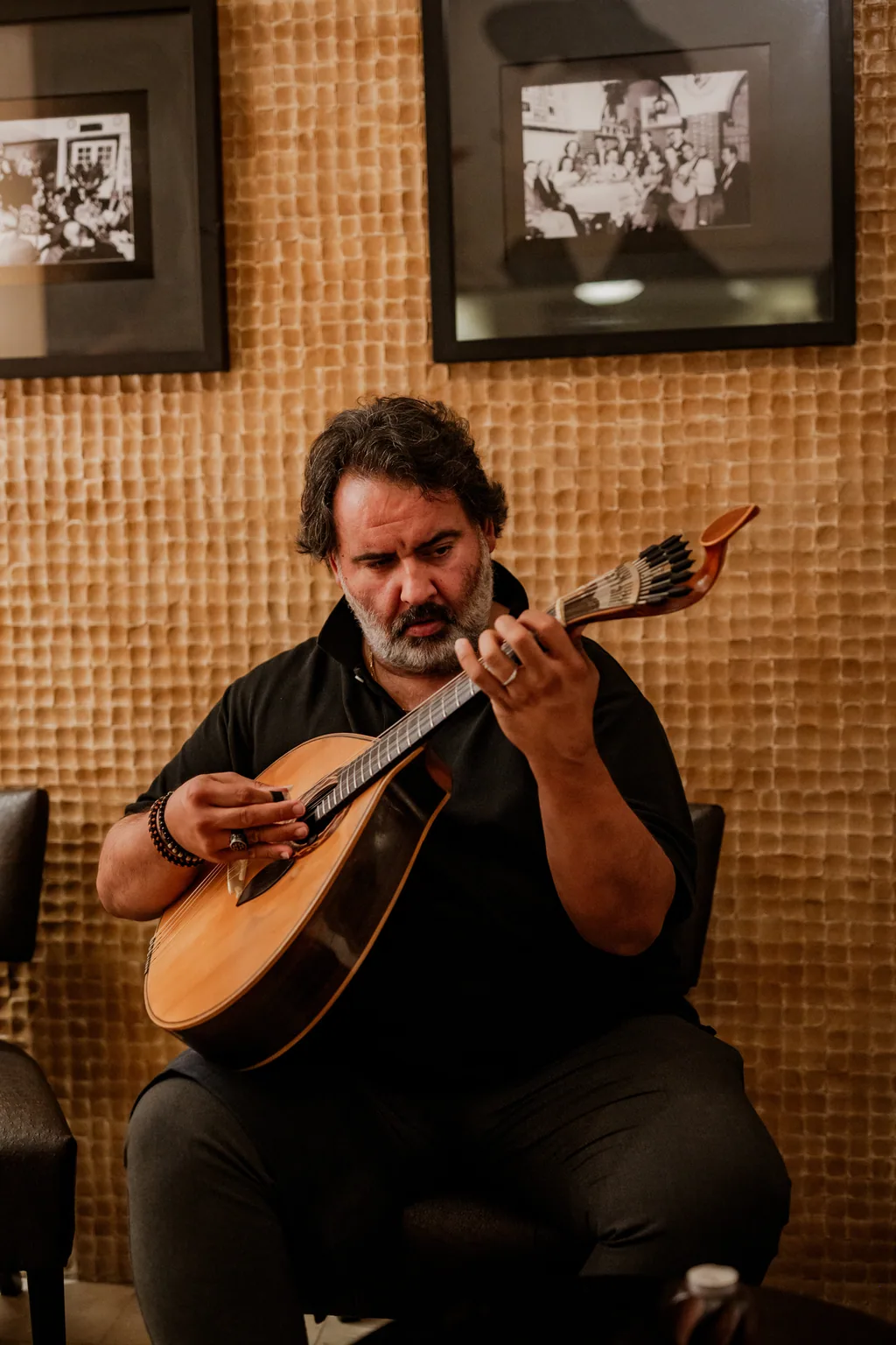 Guitarrista sentado a tocar, com retratos antigos na parede atrás