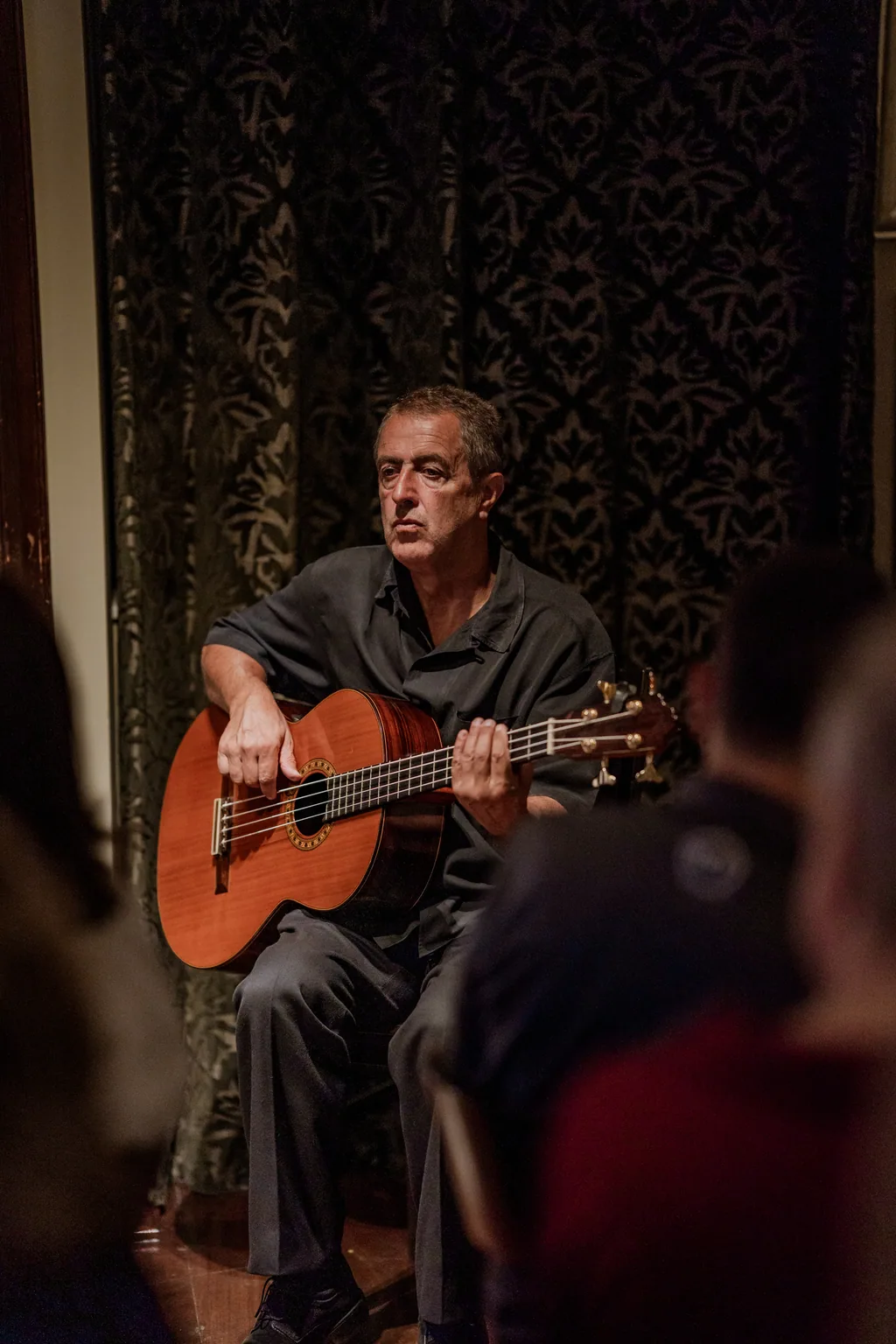 Músico a tocar viola de fado, sentado junto aos cortinados