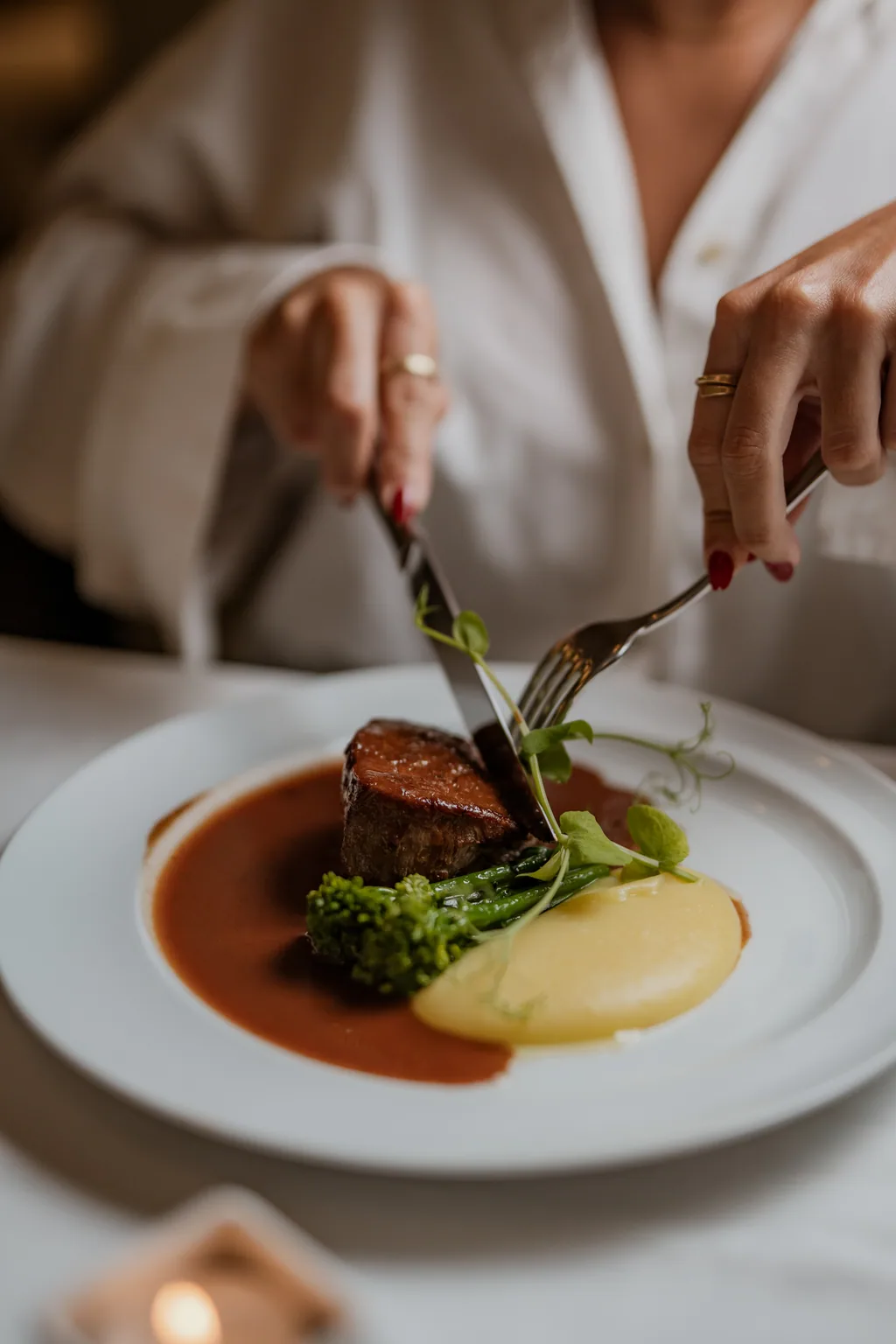 Hands cutting into the tornedos with bordelaise sauce and celeriac-apple purée