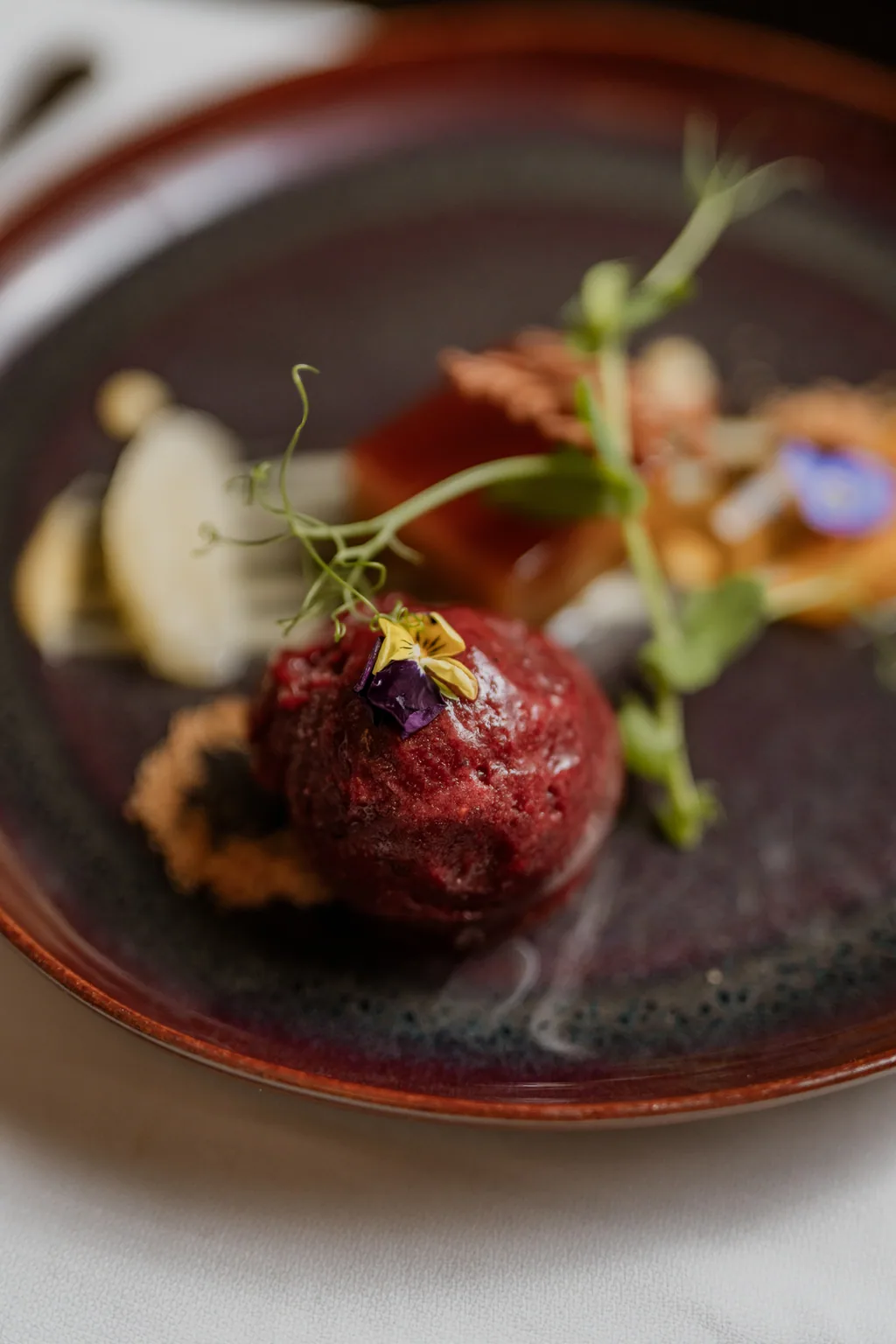Sobremesa com beterraba, frutos e flor comestível em prato de grés