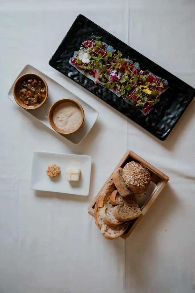 Couvert da Adega Machado: bandeja com pão, manteiga, azeitonas e entradas, servido sobre toalha branca, Lisboa