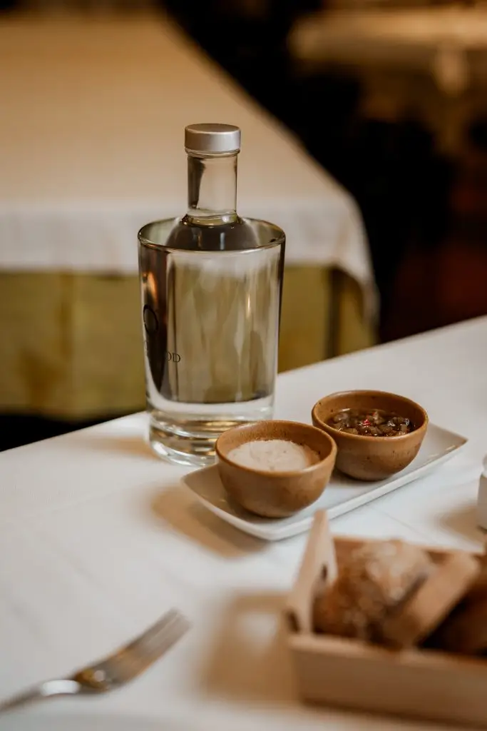 Garrafa de água e tigelas de manteiga e tapenade sobre mesa com toalha branca na Adega Machado, Lisboa