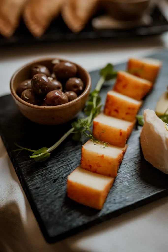 Tábua com cubos de queijo curado, queijo creme e azeitonas em ardósia preta na Adega Machado, Lisboa