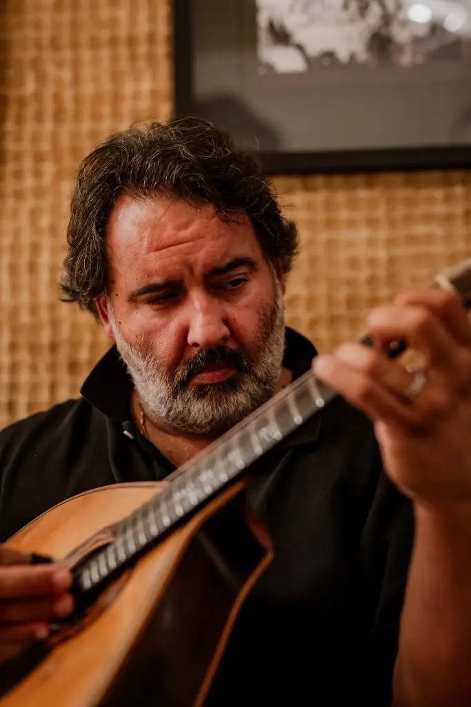 Retrato de músico a tocar guitarra portuguesa durante noite de fado na Adega Machado, Lisboa