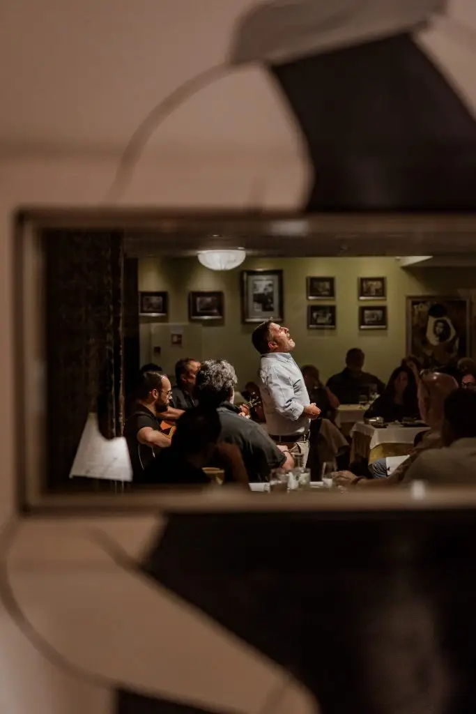 Vista da sala da Adega Machado por reflexo, com fadista a cantar e plateia a observar, Lisboa