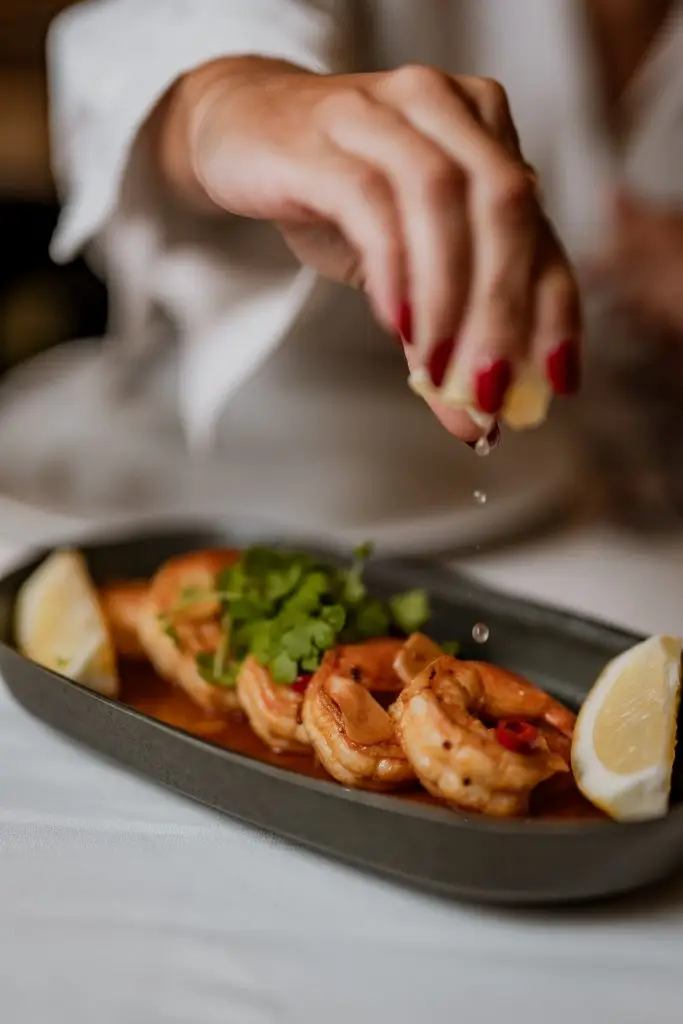 Camarão alhinho a ser temperado com limão em prato negro oval na Adega Machado, Lisboa