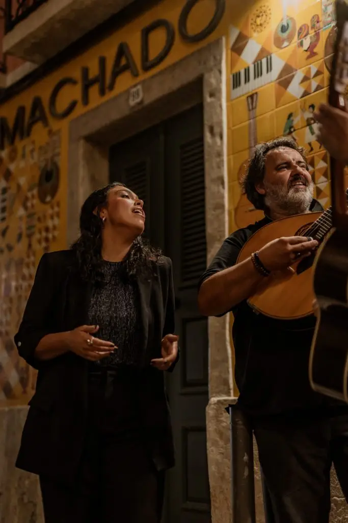 Fadista e músico cantam em frente à fachada amarela com letreiro neon ADEGA MACHADO, Bairro Alto, Lisboa