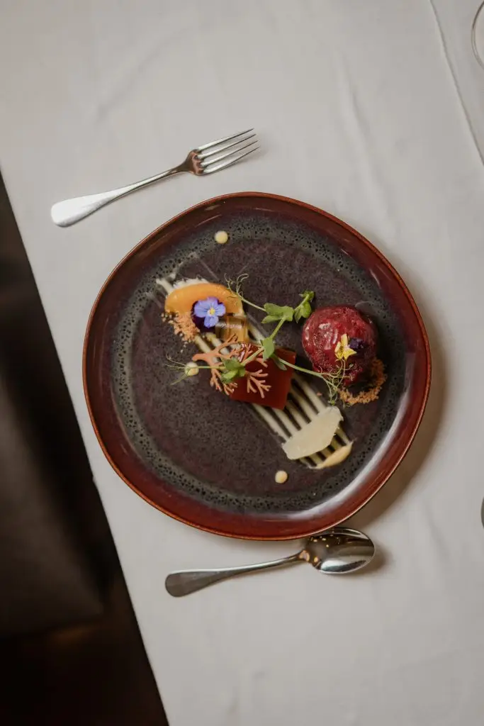 Sobremesa de fruta com flor comestível em prato cerâmico escuro na Adega Machado, Lisboa