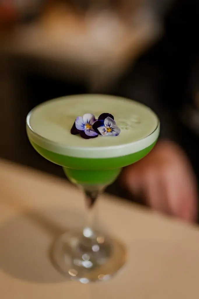 Cocktail verde com flores comestíveis em copo de margarita no bar da Adega Machado, Lisboa